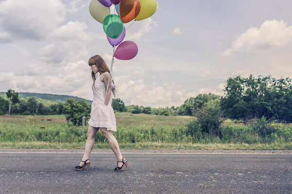  A woman walking along a road carrying a lot of colorful balloons