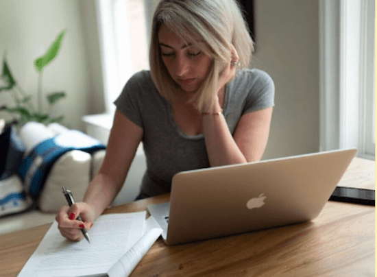 Rachel sits at a table with her laptop and printed out report, which she's reading and making notes on.