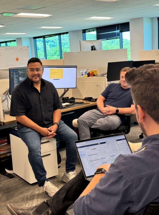 A photograph of Sergio seated on top of a filing cabinet in an office. He is surrounded by a few members of his product squad.
