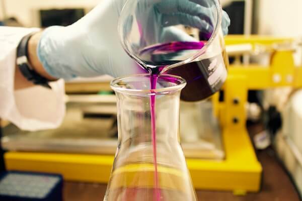 A hand pouring liquid into a beaker