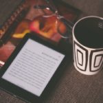 An e-reader, notebook, and pen on a couch