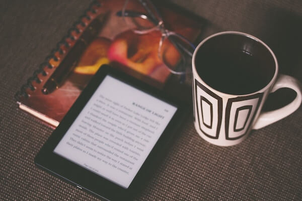 An e-reader, notebook, and pen on a couch