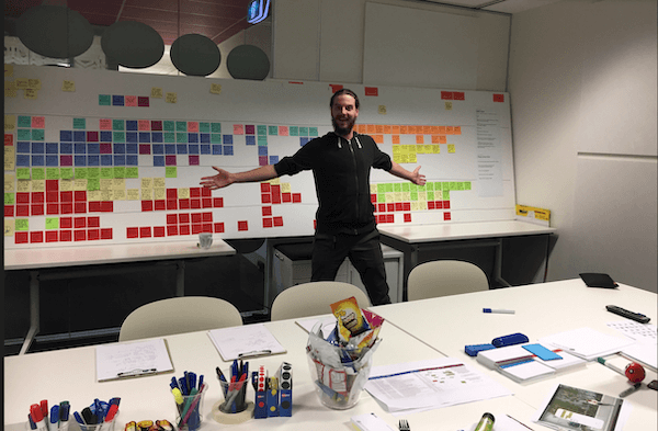 UX Designer Jamieson Hickingbotham standing in front of a white board with hundreds of sticky notes on it