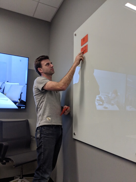 Engineer Todd Johnson is standing in front of a white board pointing at sticky notes with illustrations on them.