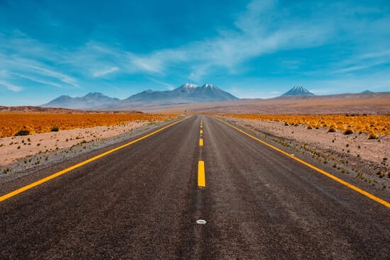 A road stretching into the horizon in the desert with mountains in the distance.