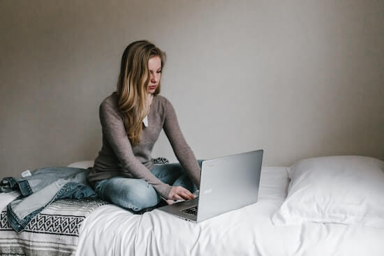 A woman is sitting on bed while working on a laptop.