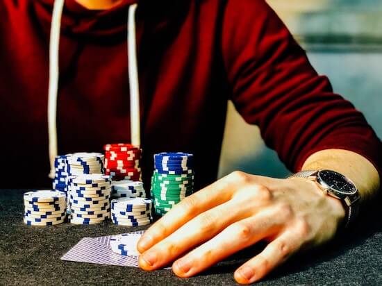 A person playing poker. They're holding a hand of cards and have a pile of poker chips in front of them.