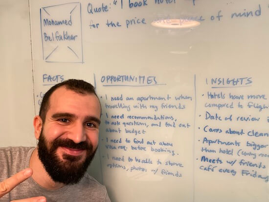 Walid stands smiling in front of a whiteboard with a list of opportunities written out, such as "I need an apartment when traveling with my friends" and "I need accommodations, to ask questions, and find out about budget."