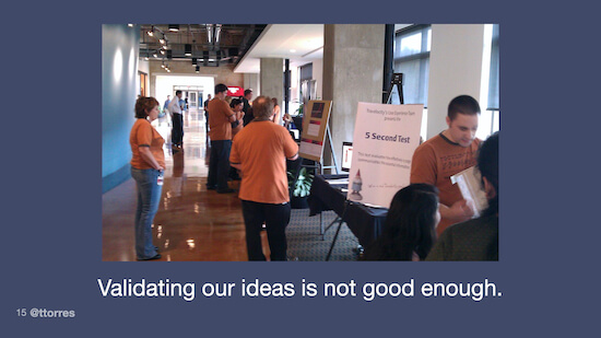 A photo of people standing around looking at different posters displayed on easels. The caption on the image reads, "Validating our ideas is not good enough."