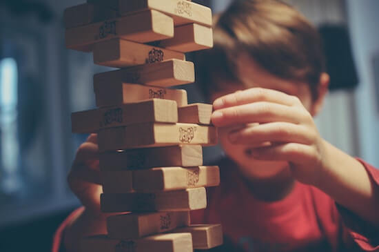 A photograph of a child playing Jenga. The small wooden blocks are precariously balanced on each other.