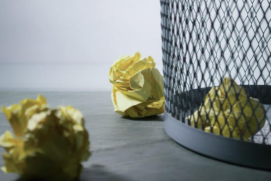 A photograph of a trash can with crumpled up pieces of paper in it.