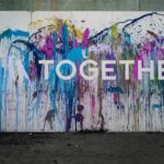 A mural on a wall with paint splatters in different bright colors. The word "together" is written in white on top of the paint.