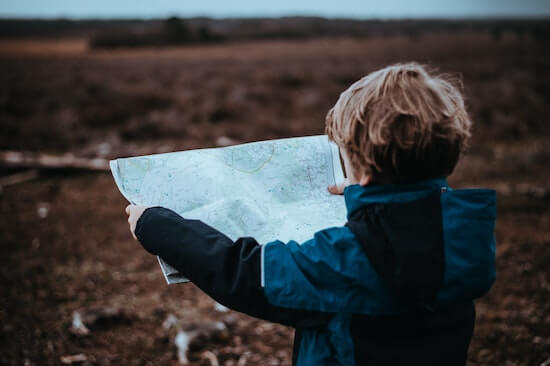 A small child is holding out a map and looking at it.