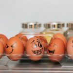 A photograph of a tray full of eggs. Each egg has a different face drawn onto it.