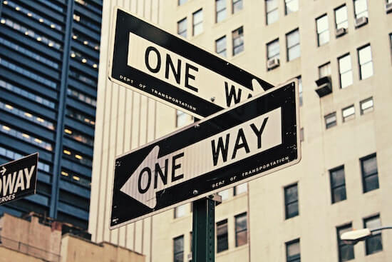 A photograph of two "one way" road signs on a street corner.