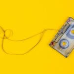 A photograph of a slightly unwound cassette tape against a yellow background.