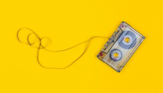 A photograph of a slightly unwound cassette tape against a yellow background.