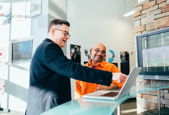 Two businessmen are looking at a laptop computer. One of them is pointing to something on the screen.