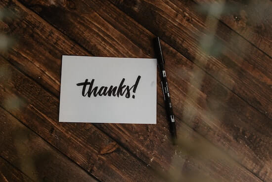 A photograph of a card and a pen on a table. The card has the word "thanks!" written in bold black letters.
