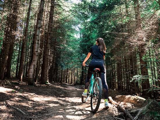 A photograph of a woman on a mountain bike on a trail in a forest.
