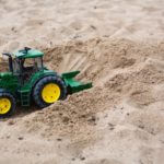 A photograph of a small bulldozer toy surrounded by sand.