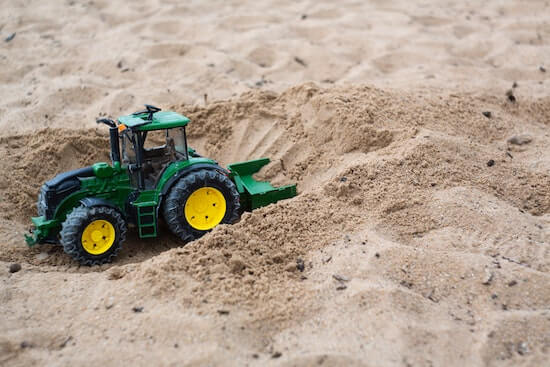 A photograph of a small bulldozer toy surrounded by sand.