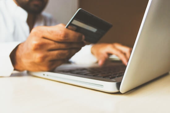 A photograph of a man sitting in front of a laptop holding a credit card.
