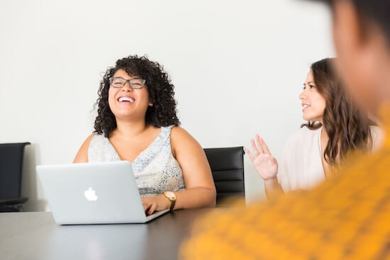 A photograph of several women sitting around a table and talking in a conference room.