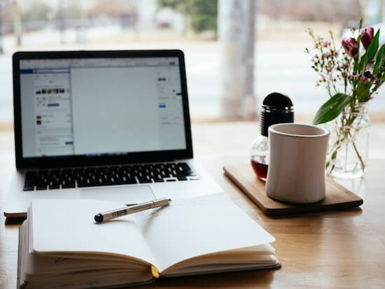 A photograph of a laptop computer on a desk with an open notebook and pen.