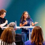 A photograph of Petra Wille and Teresa Torres standing in front of a room of people.