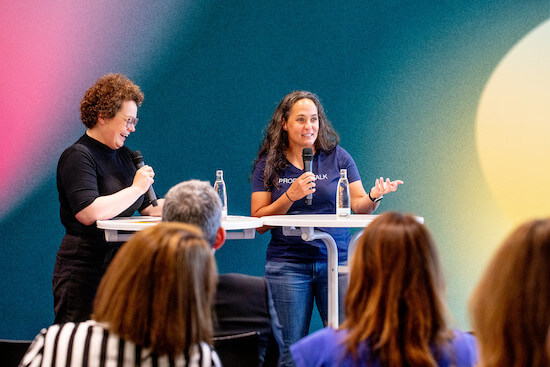 A photograph of Petra Wille and Teresa Torres standing in front of a room of people.