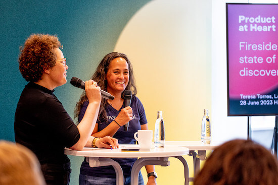 A photograph of Petra and Teresa standing in front of a room of people. Teresa is laughing.