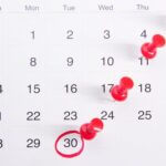 A photograph of a calendar with red pins in different days and the last day of the month circled in red pen.