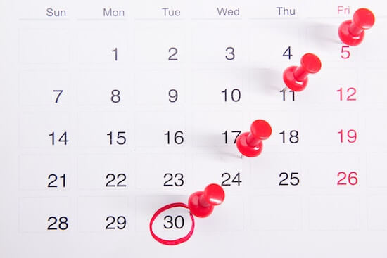 A photograph of a calendar with red pins in different days and the last day of the month circled in red pen.