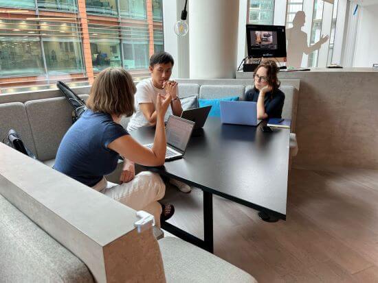 A photograph of three people sitting at a table and talking to each other.