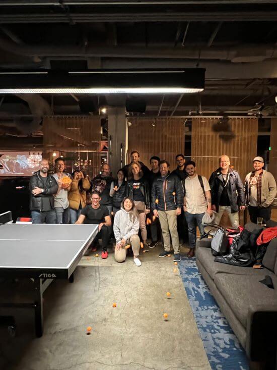 A photograph of a group of people standing in front of a ping pong table.