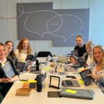 A group of people sitting around a table. Each person is holding an open copy of the Continuous Discovery Habits book.