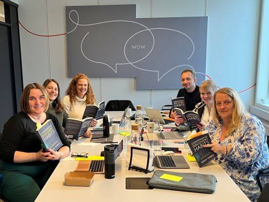 A group of people sitting around a table. Each person is holding an open copy of the Continuous Discovery Habits book.